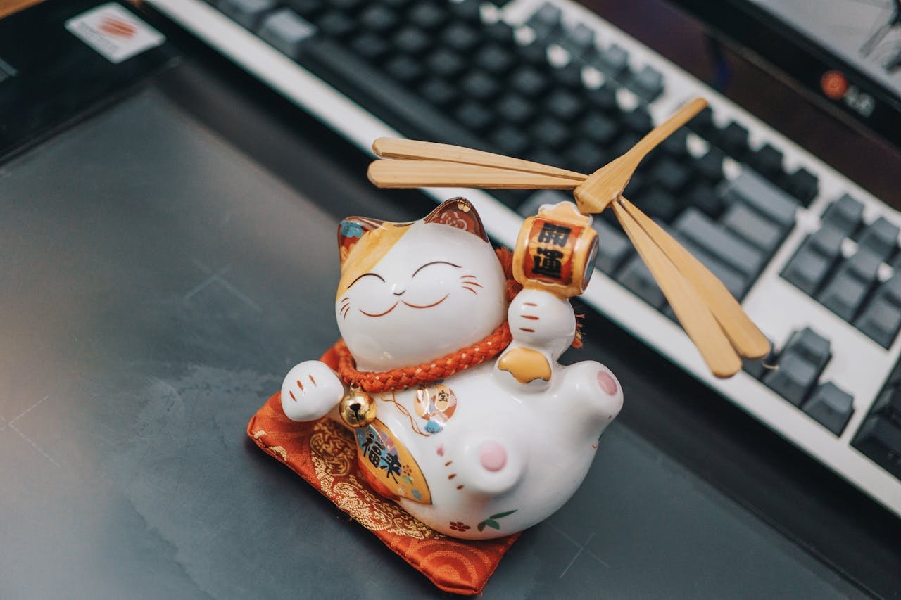 A ceramic Maneki Neko figurine sitting on a desk beside a keyboard, symbolizing luck and prosperity.